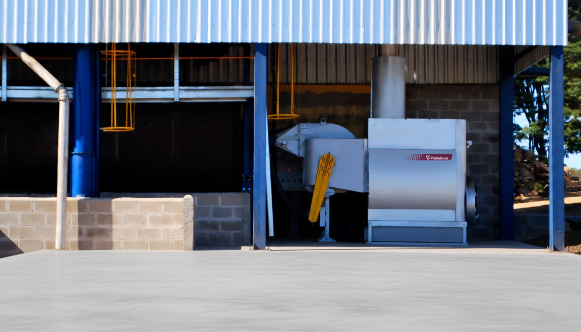 Fornalha para secador de pimenta do reino, instalada em ambiente semi aberto, com pátio asfaltado na frente.